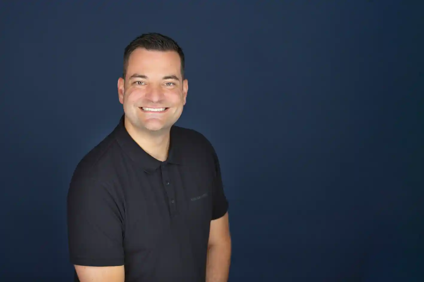 Daniel Wagner vor blauem Hintergrund Daniel Wagner schaut in die Kamera und lächelt, vor einem dunkelblauen Hintergrund